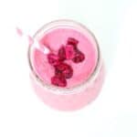 Top view of a pitaya smoothie in a glass jar topped with pieces of pitaya and a pink and white striped straw .