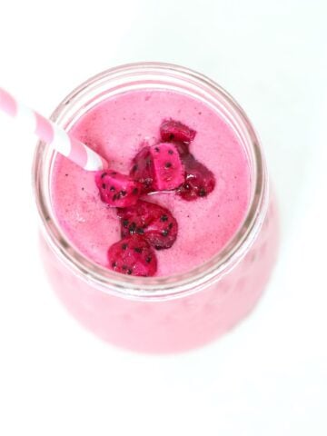 Top view of a pitaya smoothie in a glass jar topped with pieces of pitaya and a pink and white striped straw .