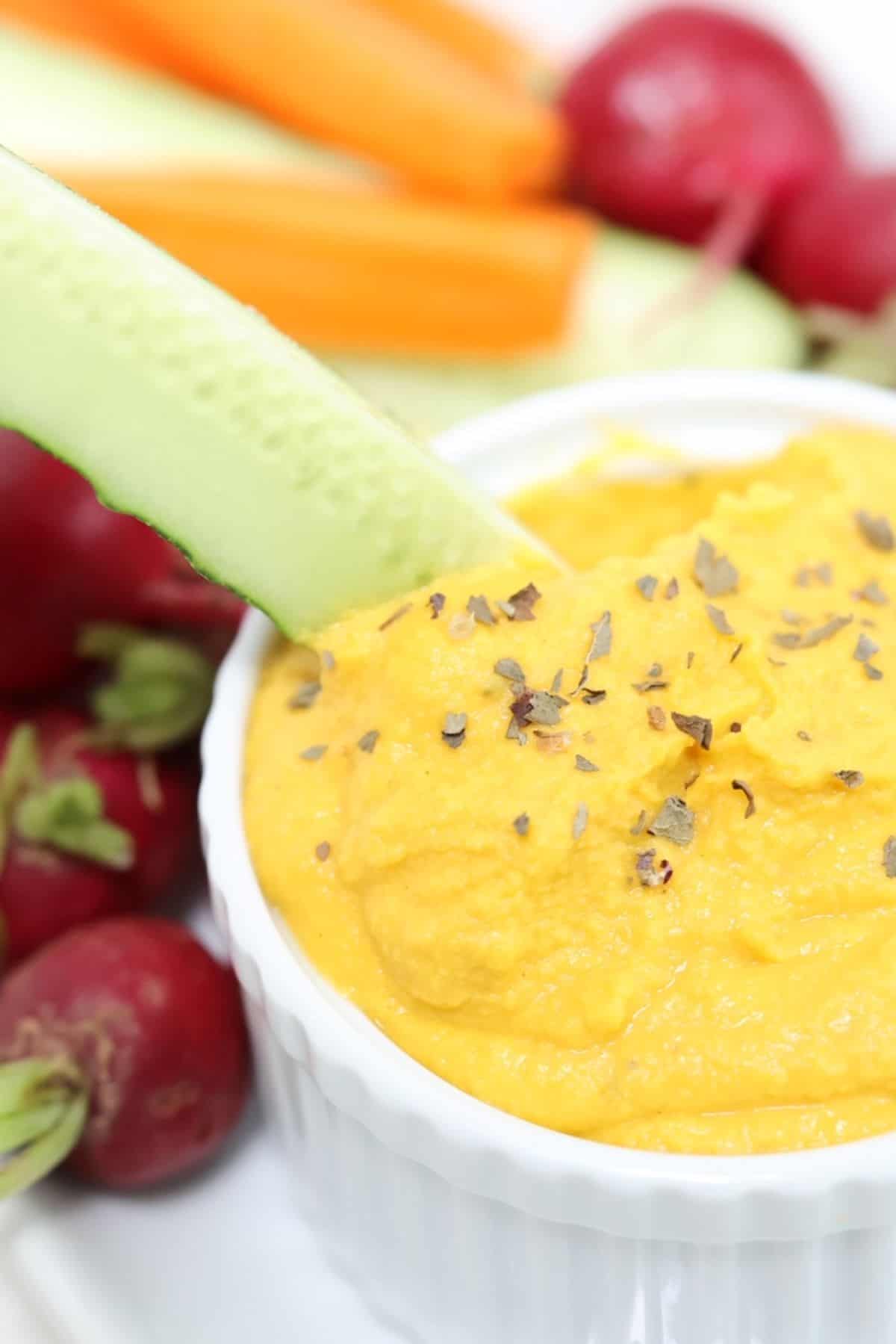 A cucumber spear being dipped into carrot hummus.