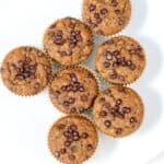 Seven Pumpkin Banana Bread muffins with mini chocolate chips on a white plate.