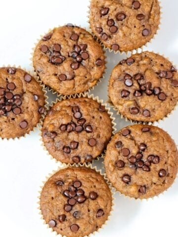 Seven Pumpkin Banana Bread muffins with mini chocolate chips on a white plate.