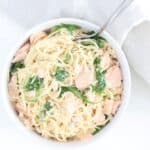 One bowl of creamy pasta with salmon and arugula in a white bowl with a fork.