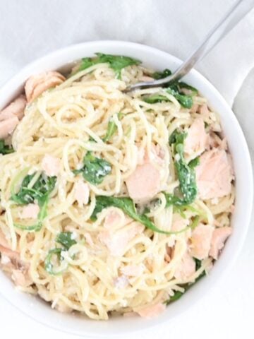 One bowl of creamy pasta with salmon and arugula in a white bowl with a fork.