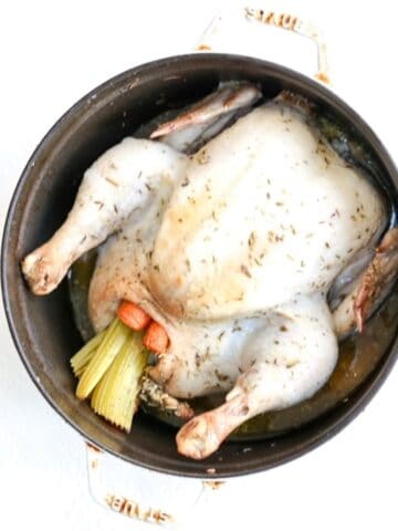 A whole roasted chicken stuffed with carrots and celery in a white Dutch oven.