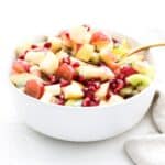 A holiday salad in a white serving bowl with a gold serving spoon.