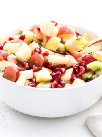 A holiday salad in a white serving bowl with a gold serving spoon.