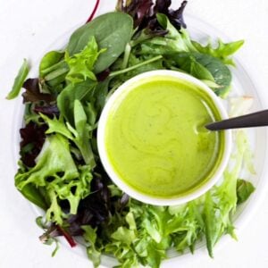 A lettuce salad on a round white plate with a small white bowl of basil balsamic dressing.