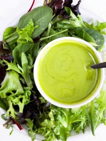 A lettuce salad on a round white plate with a small white bowl of basil balsamic dressing.