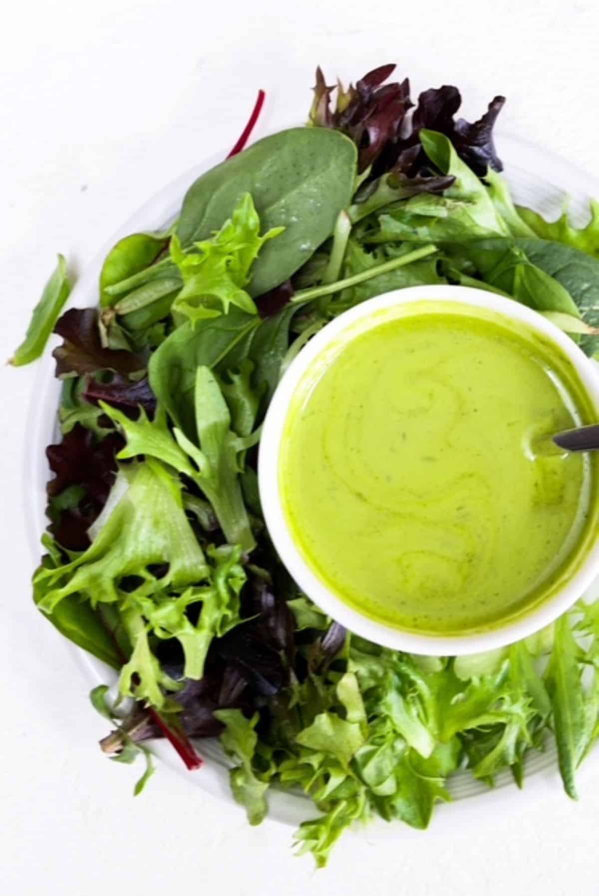 A small bowl of Basil Balsamic Dressing with a simple lettuce salad on a white plate.