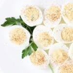 Nine deviled eggs on a white plate with a sprig of fresh parsley for garnish.