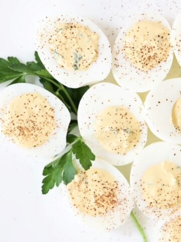 Nine deviled eggs on a white plate with a sprig of fresh parsley for garnish.