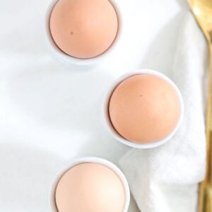 Three brown hard-boiled eggs in white egg cups.