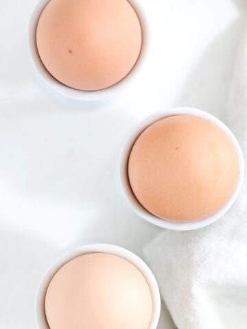 Three brown hard-boiled eggs in white egg cups.