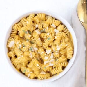 A bowl of pasta with butternut squash pasta sauce with a golden spoon to the right of the bowl.