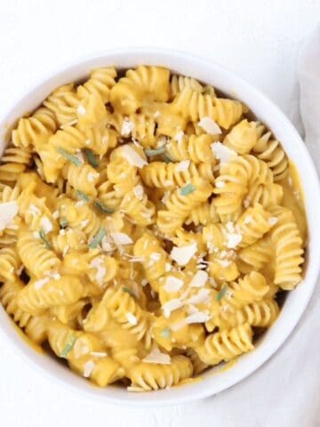 A bowl of pasta with butternut squash pasta sauce with a golden spoon to the right of the bowl.
