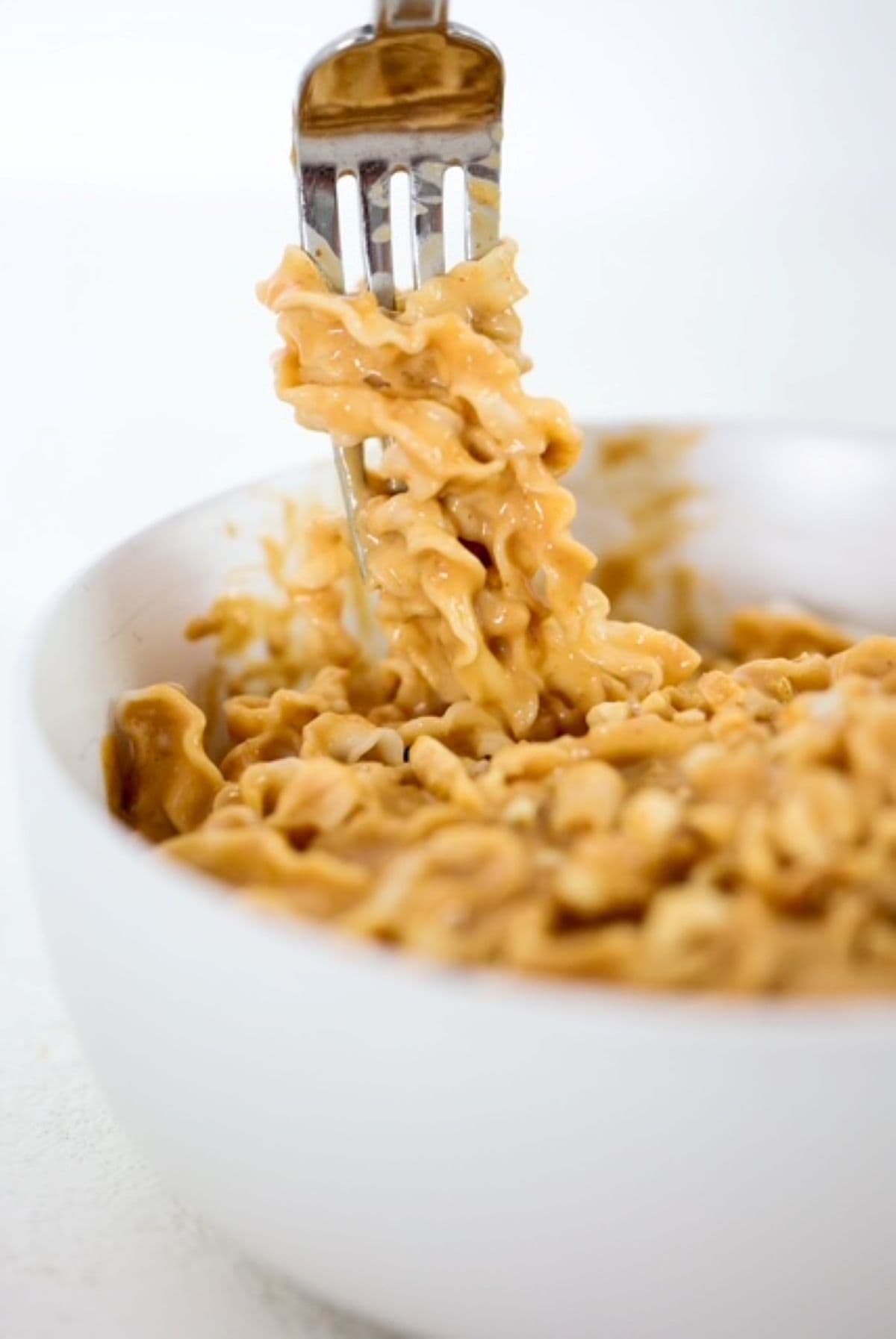 A fork with noodles wrapped around it coming out of a bowl of noodles in a peanut butter sauce.