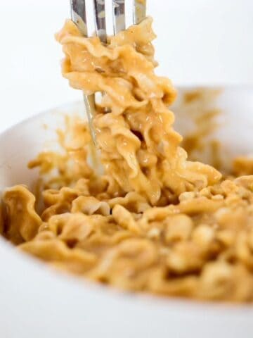 A bowl of noodles in a peanut butter sauce with some wrapped around the prongs of a fork.