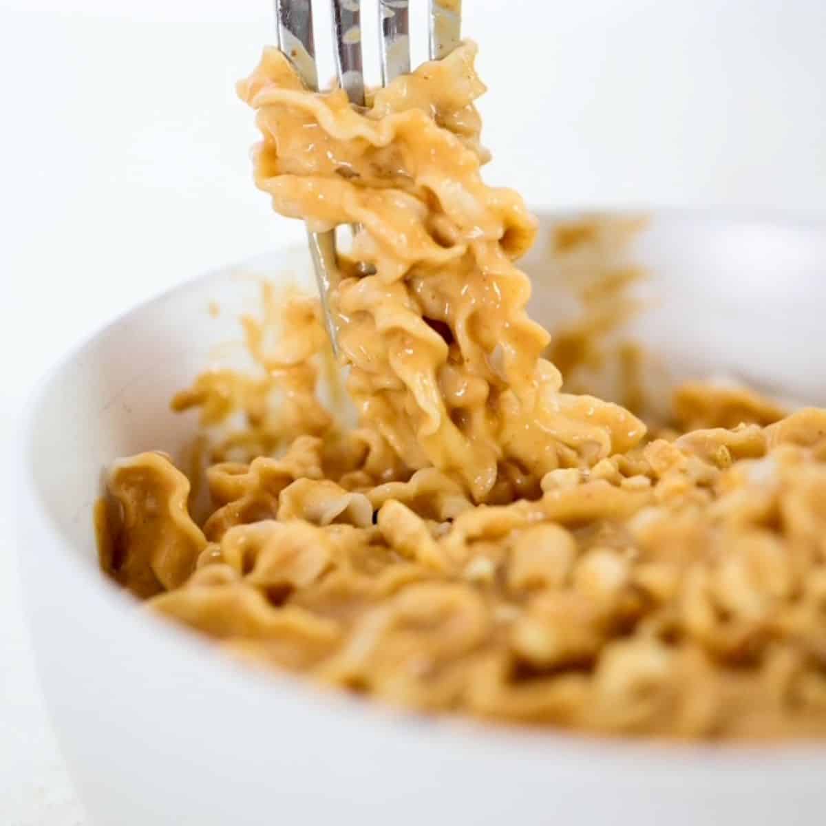 A bowl of noodles in a peanut butter sauce with some wrapped around the prongs of a fork.