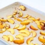 Roasted peach slices on a lined baking sheet.
