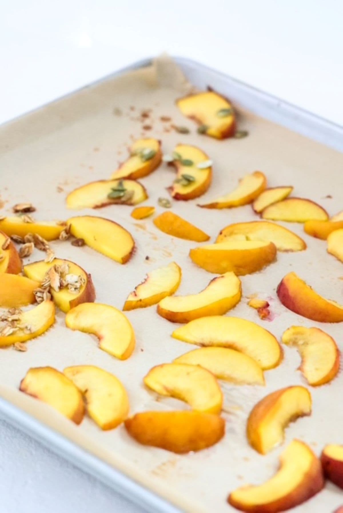 Sliced roasted peaches on a lined baking sheet.