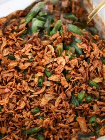 Green Bean Casserole in a white, square baking dish with a serving spoon.