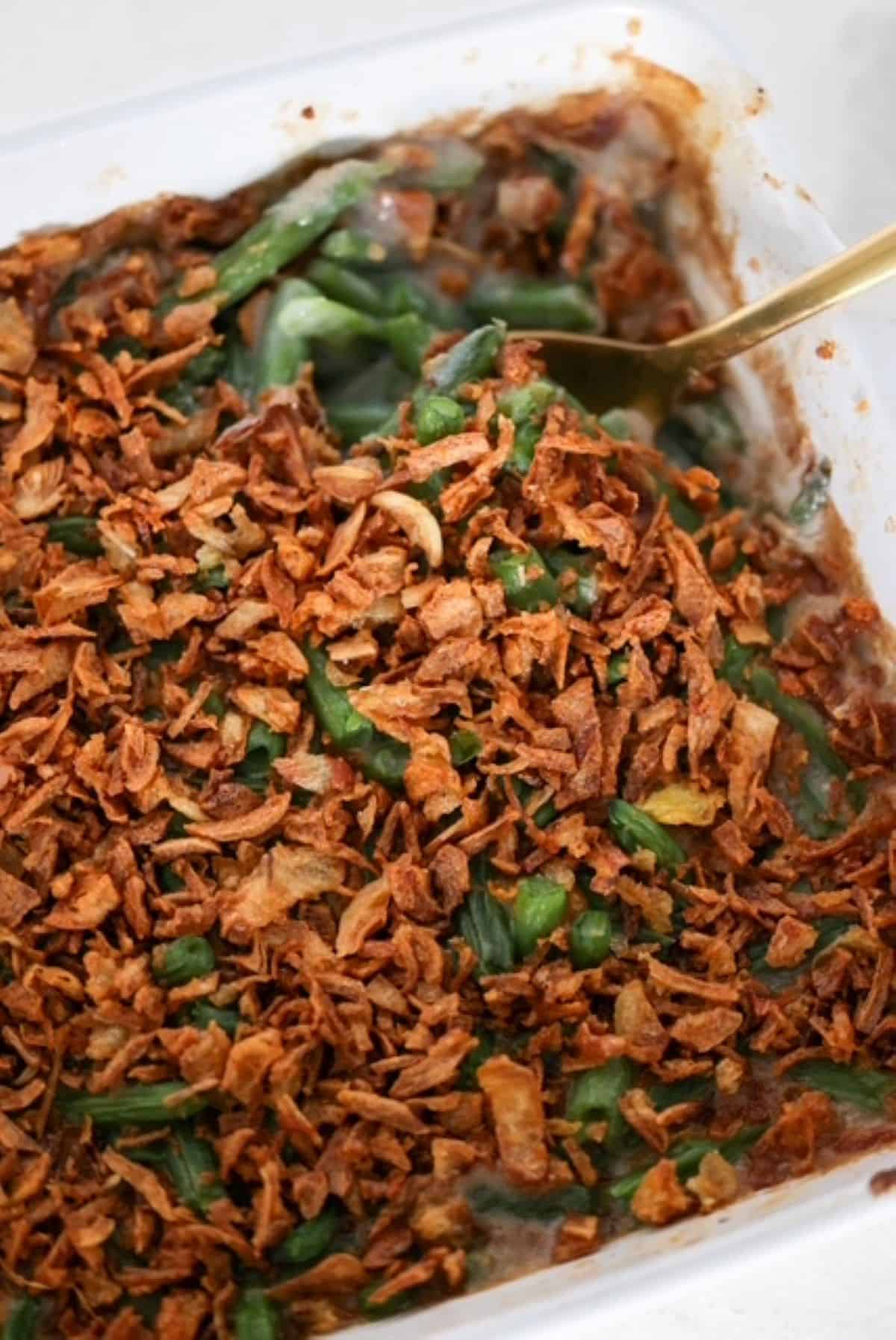 Green Bean Casserole in a white baking dish with a serving spoon.