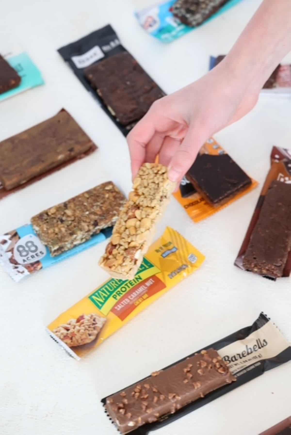 A variety of protein bars out of their packages with a child's hand grabbing one.
