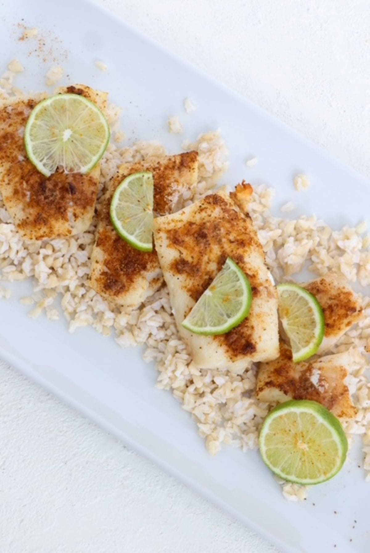 Cooked cod fillets topped with seasoning and fresh lime slices on a white serving dish.