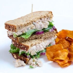 Two halves of a tuna and chickpea salad stacked with a toothpick through the center with a side of sweet potato chips.