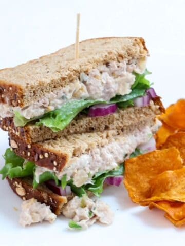 Two halves of a tuna and chickpea salad stacked with a toothpick through the center with a side of sweet potato chips.