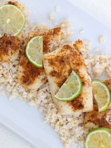 Air-fried cod topped with seasoning and slices of fresh lime on a white dish.