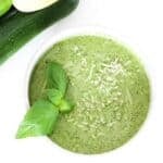 Zucchini pesto in a white bowl topped with fresh basil leaves.