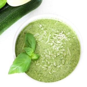 Zucchini pesto in a white bowl topped with fresh basil leaves.