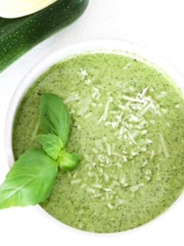 Zucchini pesto in a white bowl topped with fresh basil leaves.