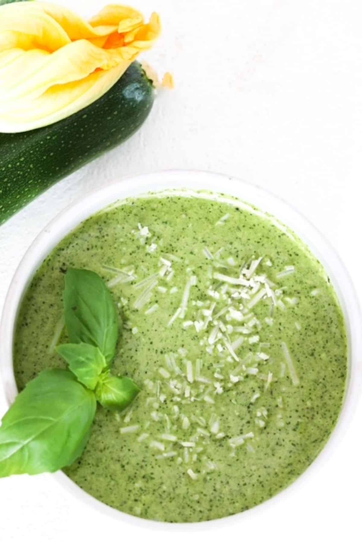 Zucchini pesto in a white bowl topped with fresh basil leaves.