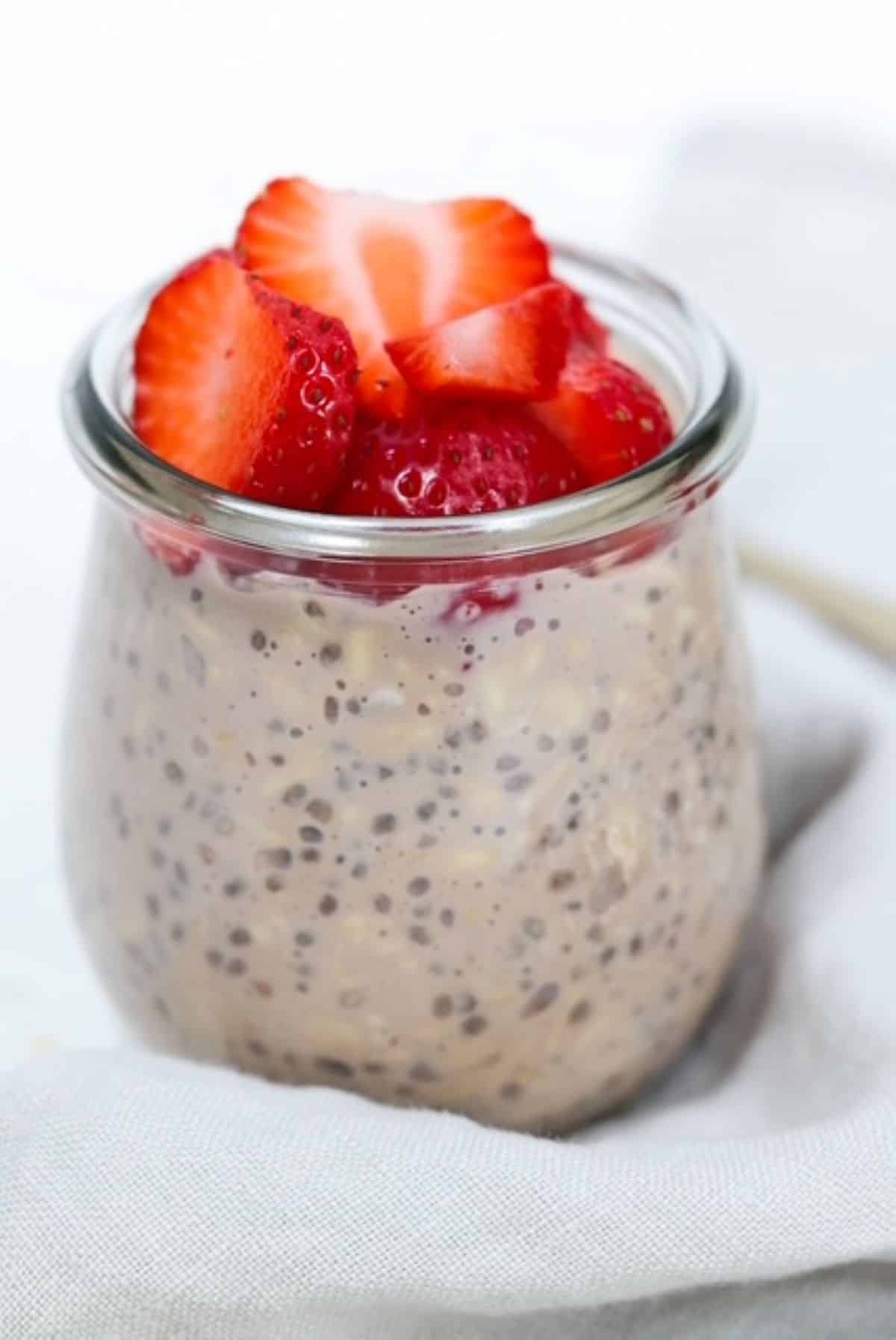 Chocolate overnight oats in a small glass jar topped with sliced strawberries.