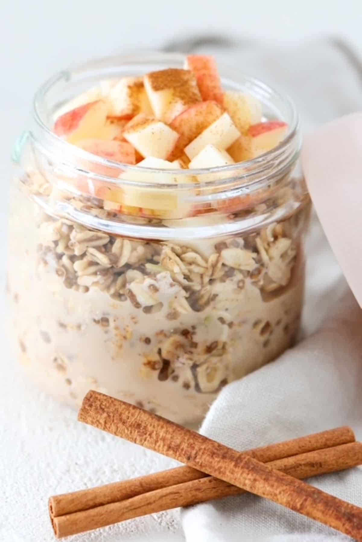 Apple Cinnamon Overnight Oats in a glass jar with cinnamon sticks in front of it.