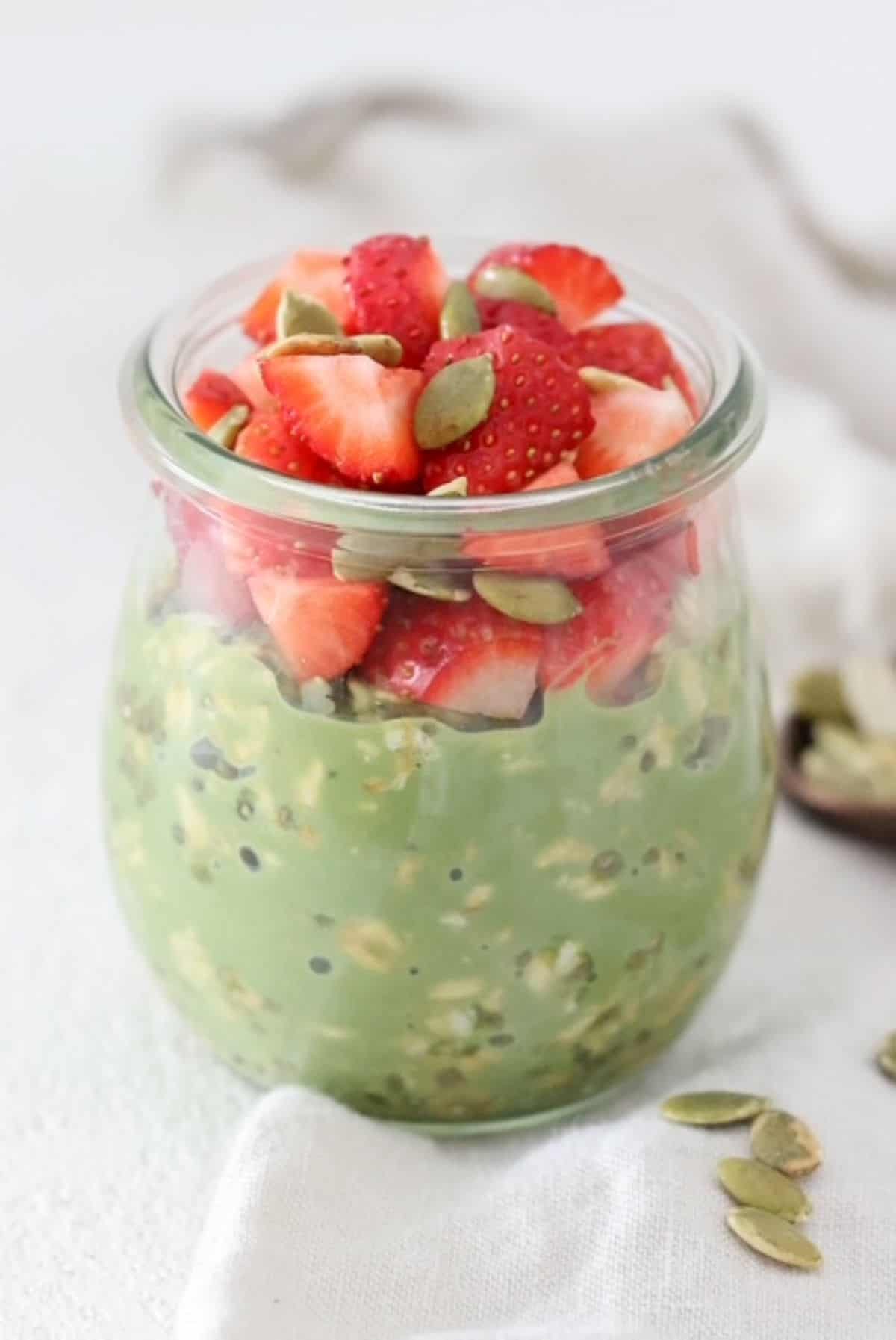 Matcha overnight oats topped with fresh strawberries in a glass jar.