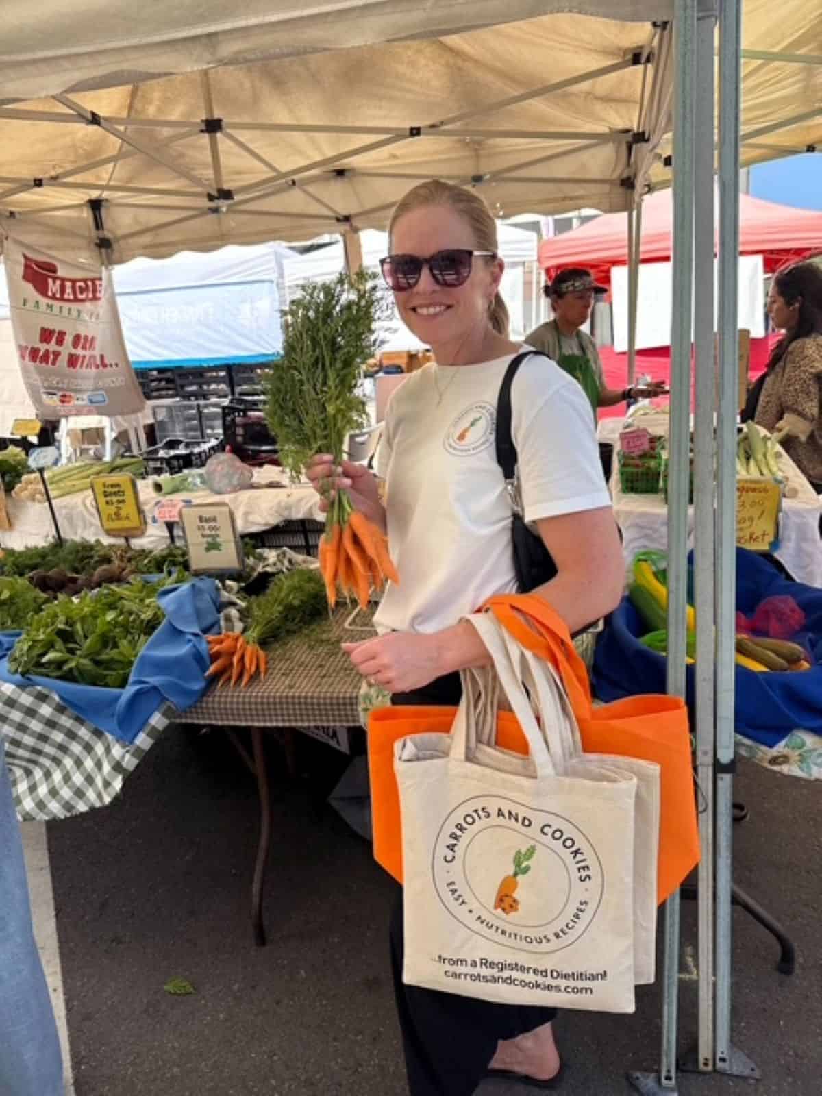 Kristi Ruth RD of Carrots & Cookies holding one bunch of carrots at a farmer's market.