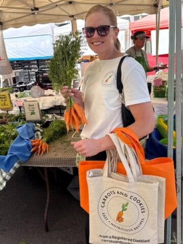 Kristi Ruth RD of carrotsandcookies.com at a farmer's market holding one bunch of carrots.