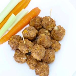 Buffalo Chicken Meatballs on a plate with carrot and celery sticks.