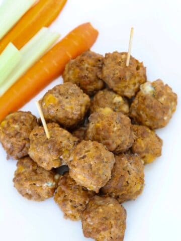 Buffalo Chicken Meatballs on a plate with carrot and celery sticks.